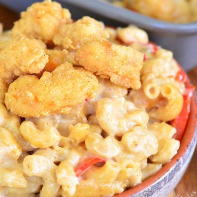 blue and orange clay bowl filled with po'boy mac and cheese on a woosen table with a baking pan and more mac and cheese.