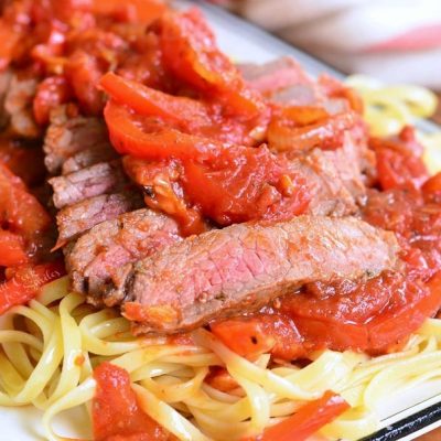 decorative white rectangular plate with steak pizzaiola linguine on a wooden table as viewed close up