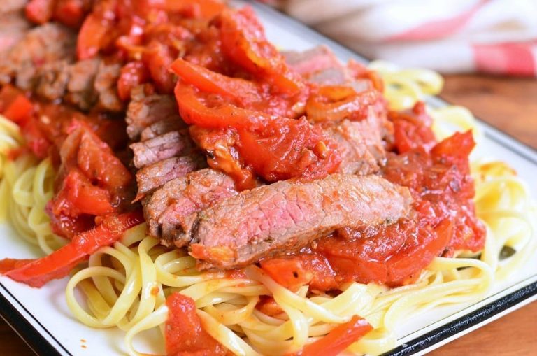 decorative white rectangular plate with steak pizzaiola linguine on a wooden table as viewed close up