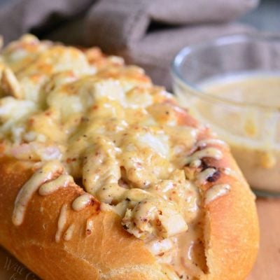 White BBQ chicken sub on a wooden table with a small glass dish holding white BBQ sauce in the background as viewed close up