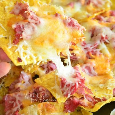 Baking sheet tray filled with reuben nachos with a hand pulling out 1 chip covered in toppings