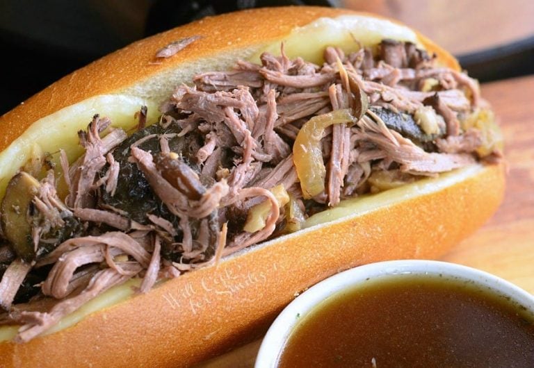 large hogie roll covered in cheese filled with slow cooker mushroom and onion italian beef on a wooden table as viewedclose up.