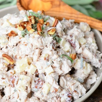 White bowl filled with pecan, sage and gruyere turkey salad on a cord trivet with wooden spoons in the background.