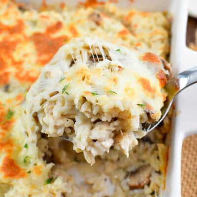 scooping creamy cheesy chicken rice casserole with silver spoon.