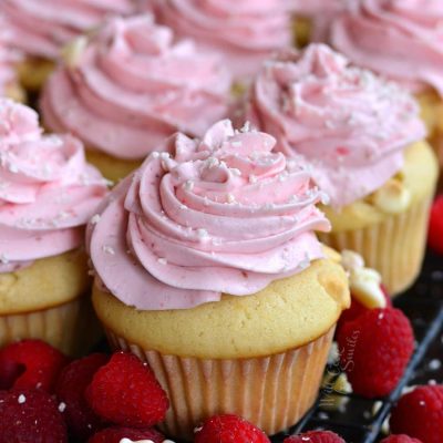 vanilla cupcake with pink raspberry frosting on top and white chocolate shavings.