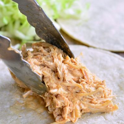 Putting shredded chicken on a soft tortilla with tongs.