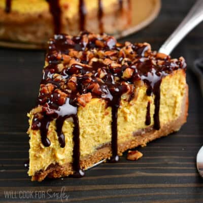 slice of pumpkin cheesecake on a serving spatula topped with chocolate and pecans.