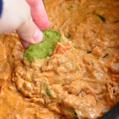 dipping a green tortilla chip into the enchilada dip.