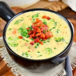 black bowl filled with broccoli cheese soup topped with crispy bacon and chives.