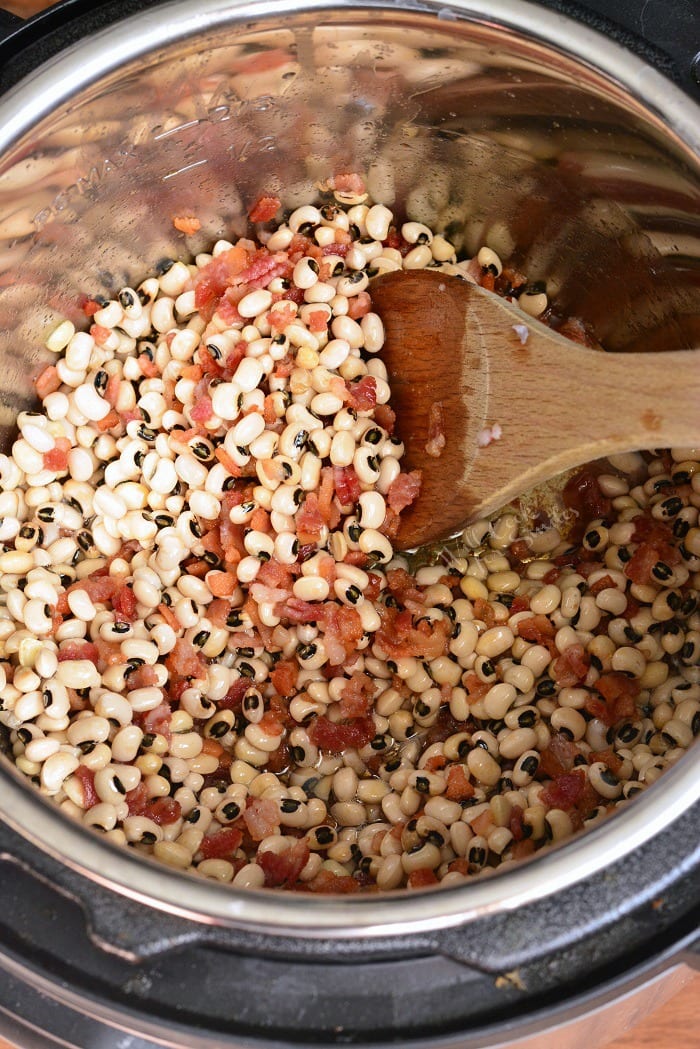 stirring Instant Pot Black Eyed Peas and Bacon with a wooden spoon 