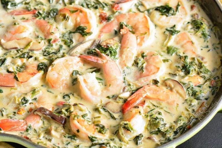 shrimp nestled into the creamy spinach and mushroom sauce in a pan.