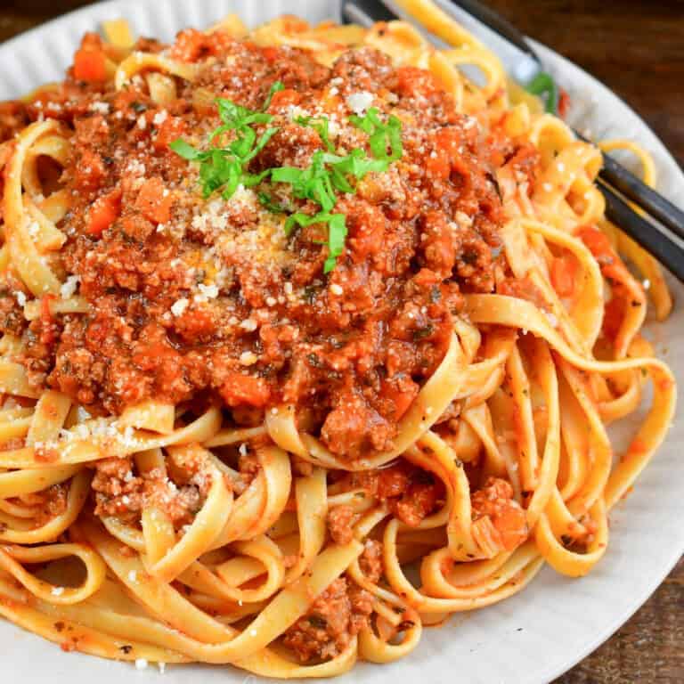 fettuccine pasta mixed and topped with a tomato based meat sauce on a plate.