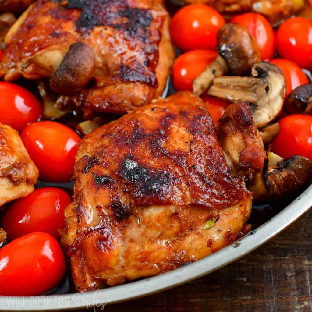 deep golden baked balsamic chicken thighs in a pan with tomatoes and mushrooms.