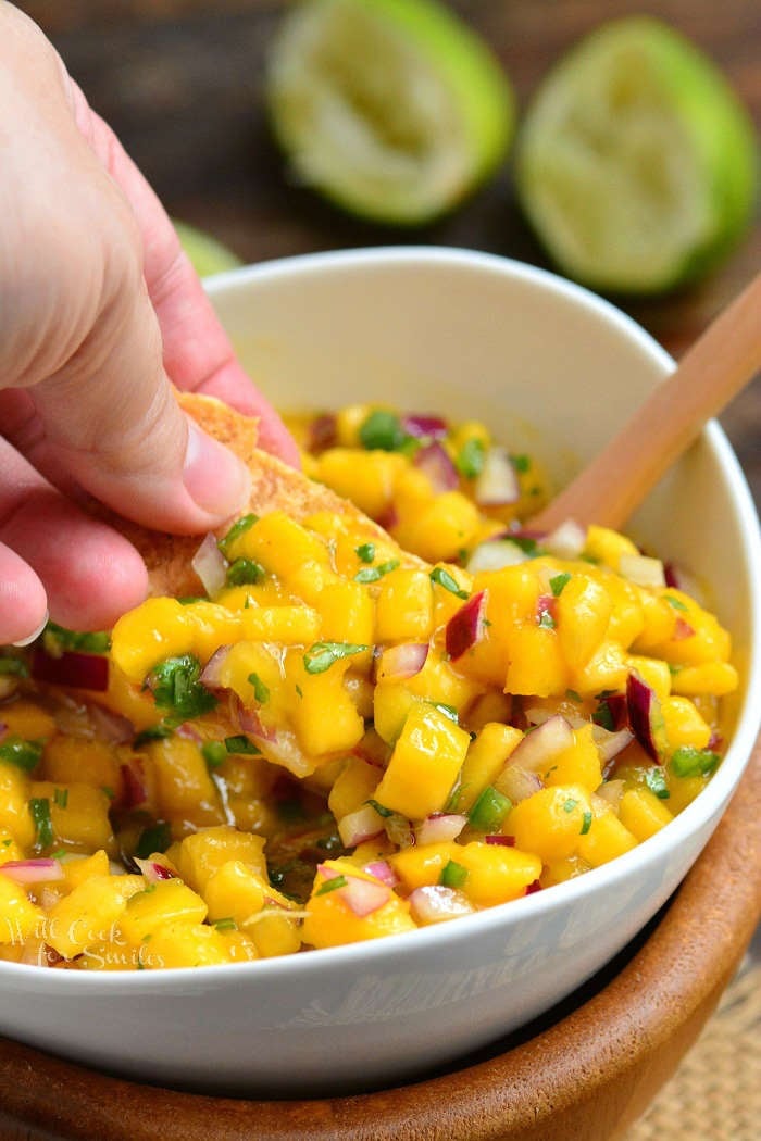 mango salsa in a white bowl being scooped with a chip. 