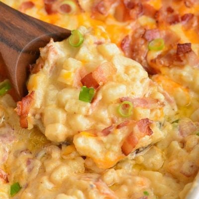 close-up of scooping cheesy potato casserole with wooden spoon.