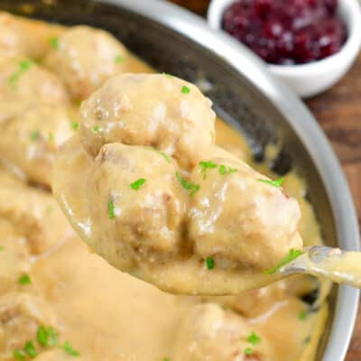 holding three meatballs in creamy sauce on a large metal spoon over the pan.