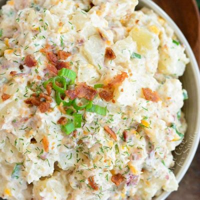 above view on ready potato salad in a bowl with green onion and bacon bits on top and spoon next to the bowl