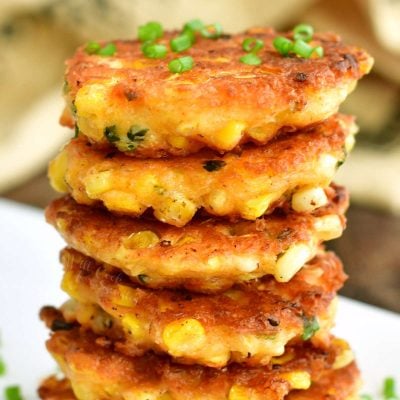 closer view of fried corn fritters stacked on top of each other and some chives on top