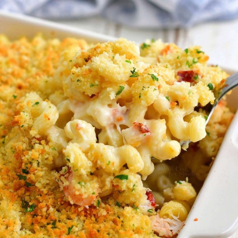 closer view of spoon pulling out some baked mac and cheese out of the baking dish with lobster pieces throughout