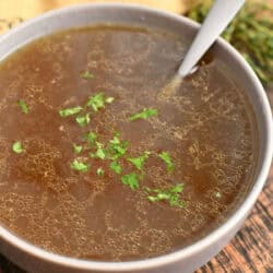 beef stock in a soup bowl with a spoon and parsley for garnish.