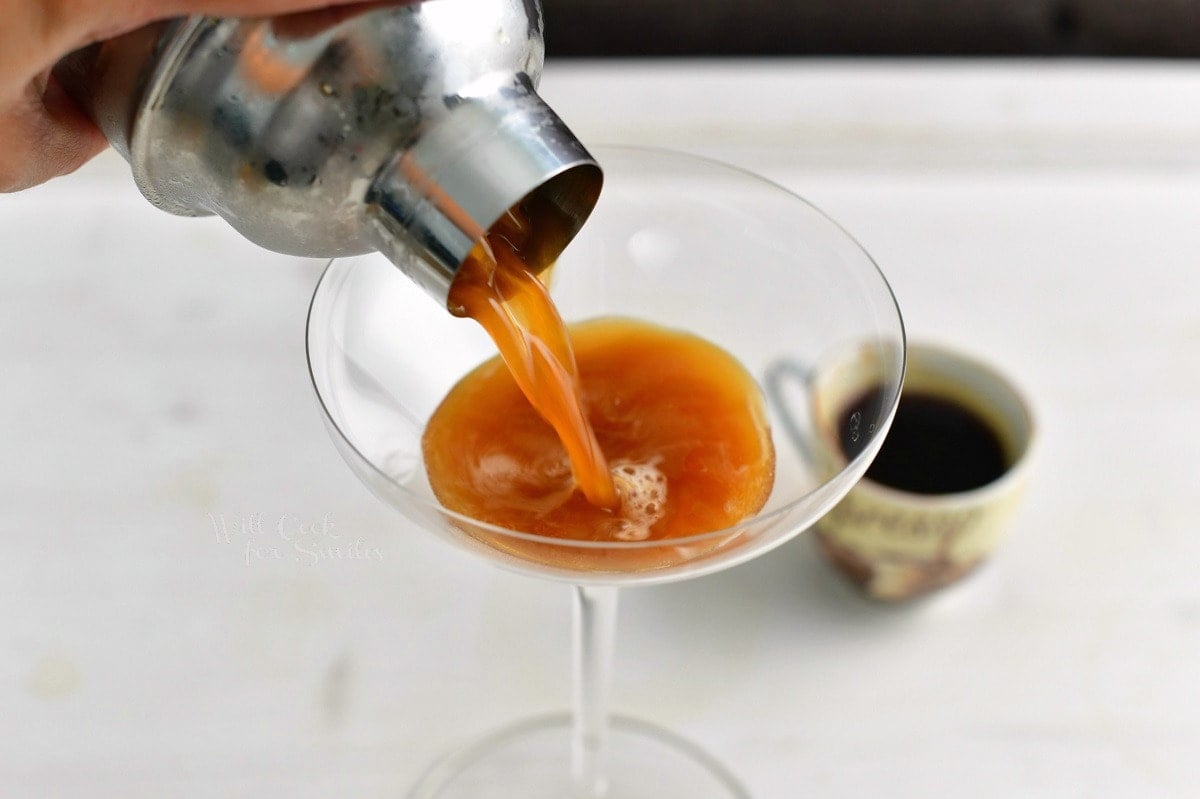 pouring the light brown cocktail into the martini glass