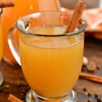 hot apple cider in glass mug garnished with cinnamon stick