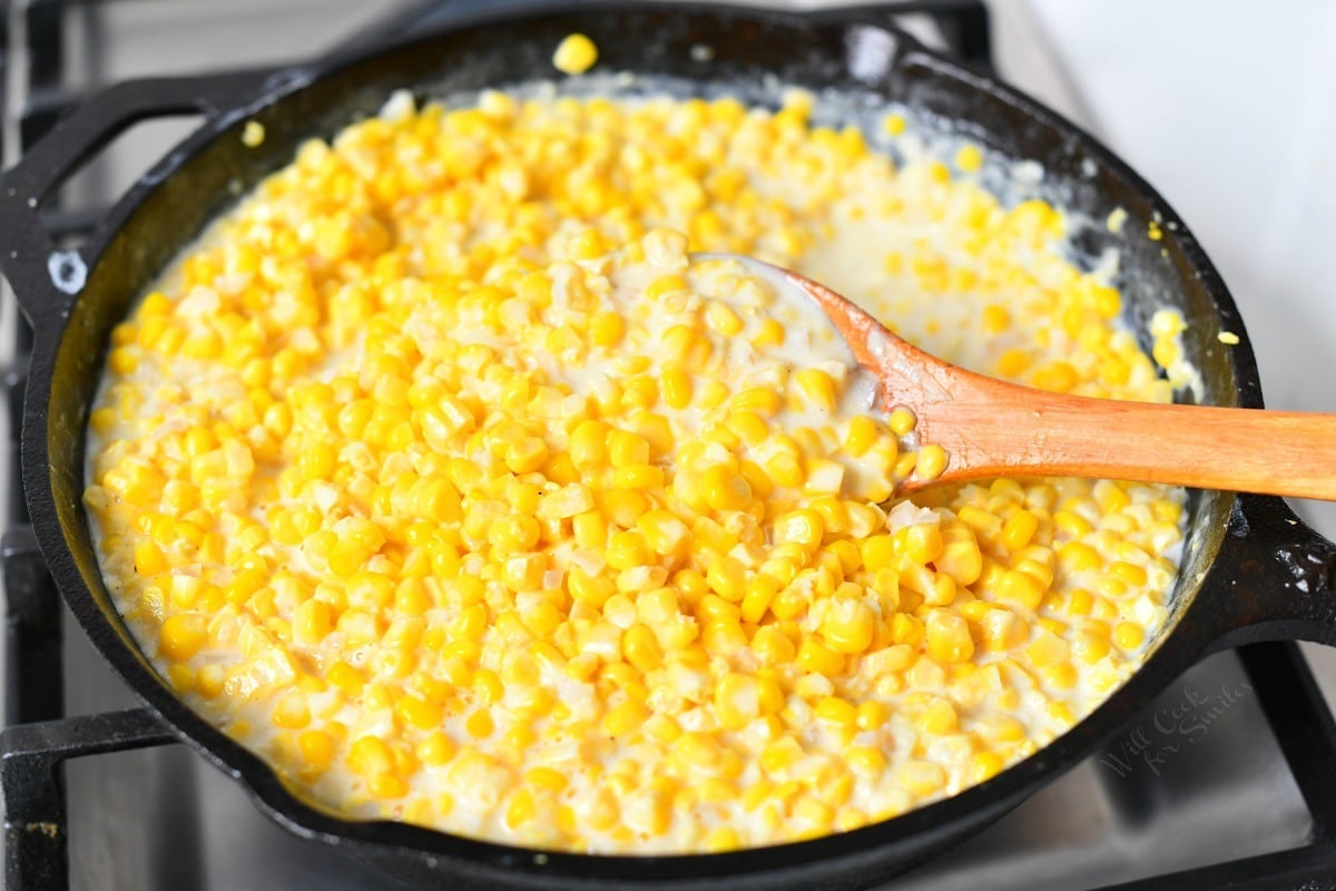 wooden spoon stirring creamed corn in cast iron skillet