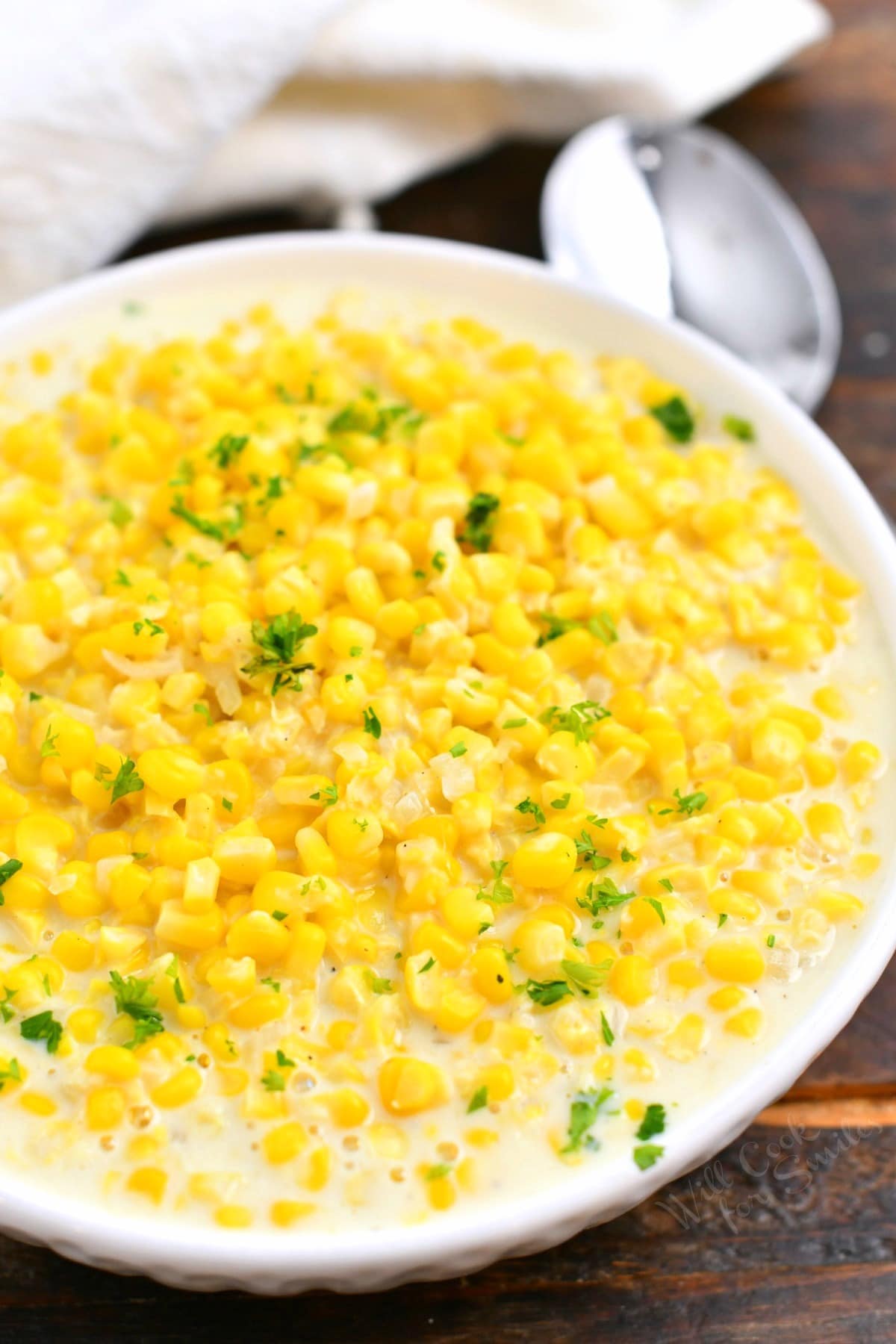 yellow corn vegetable side dish in a white bowl garnished with fresh parsley