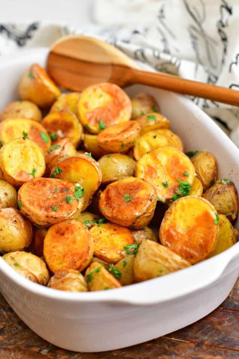 wooden spoon in white casserole dish with roasted potatoes