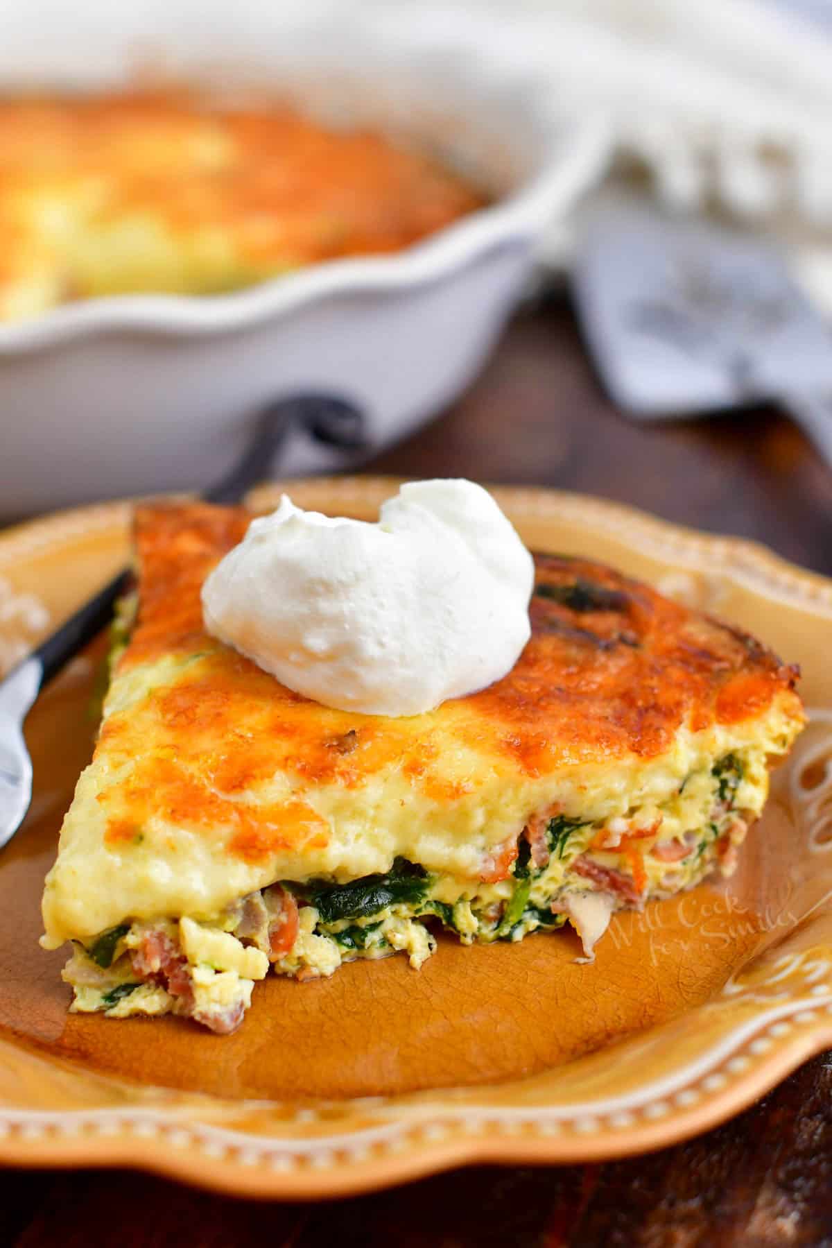 A slice of crustless quiche placed on a brown plate with a dollop of sour cream on top.