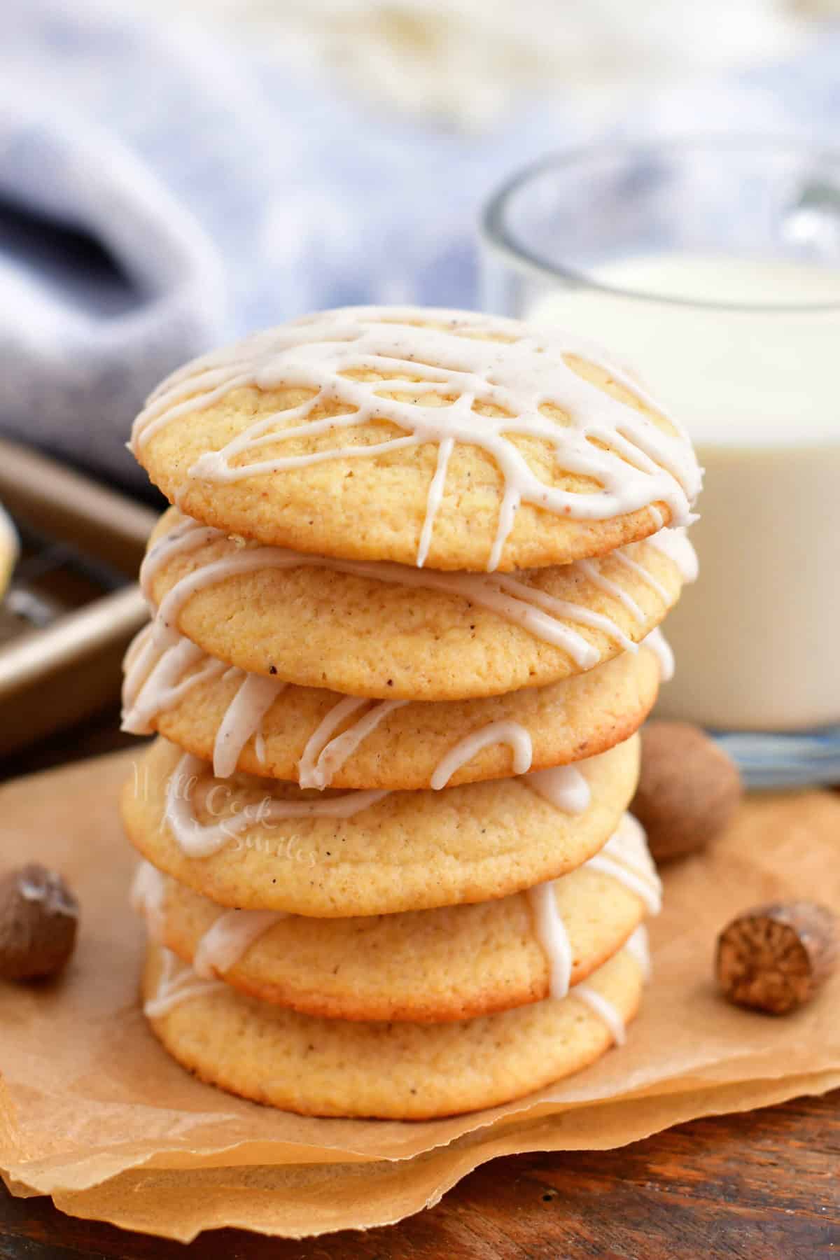 Eggnog cookies are stacked on an orange napkin, next to a glass of milk.