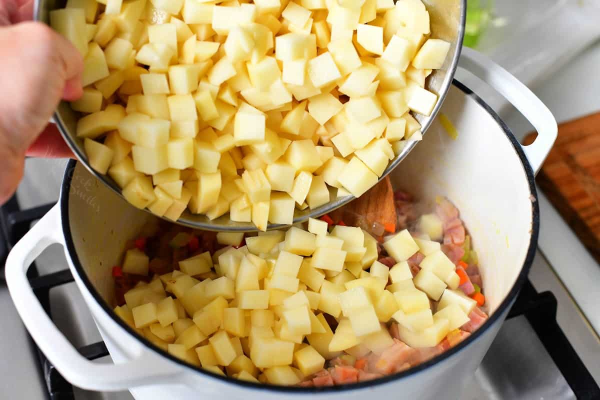 adding diced potatoes into a pot of ham soup