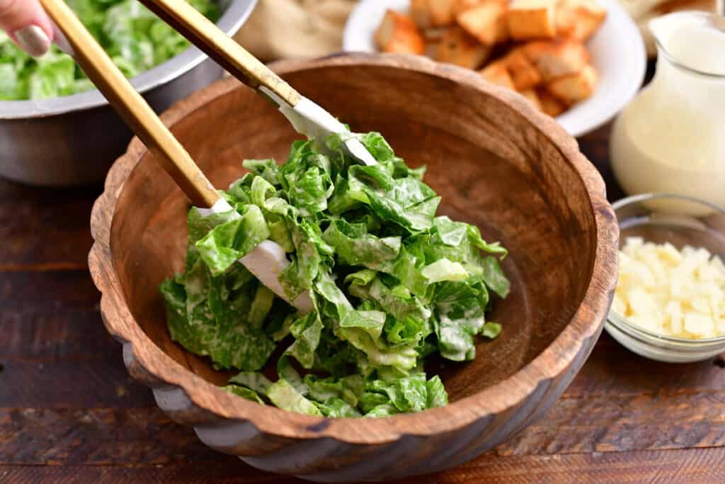 using tongs to serve salad into small bowl