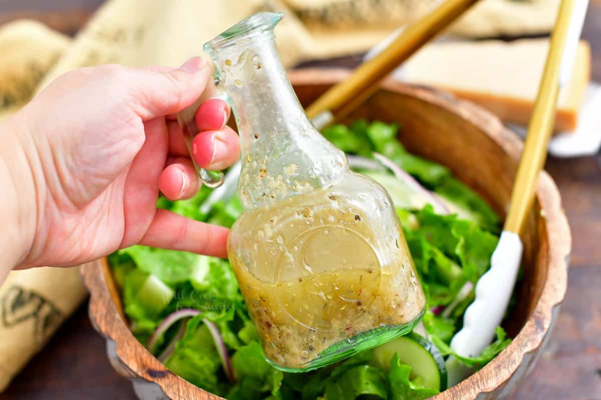 closeup: woman's hand holding bottle of homemade Italian dressing; bowl of salad in background
