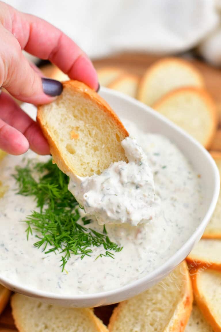 close up image: dipping toasted bread into bowl with salmon cream cheese dip