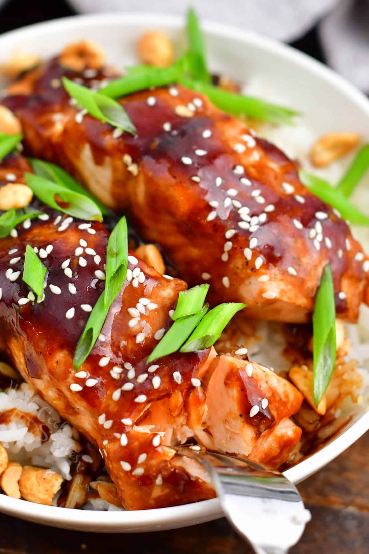 closeup: metal fork flaking teriyaki salmon in a bowl of white rice