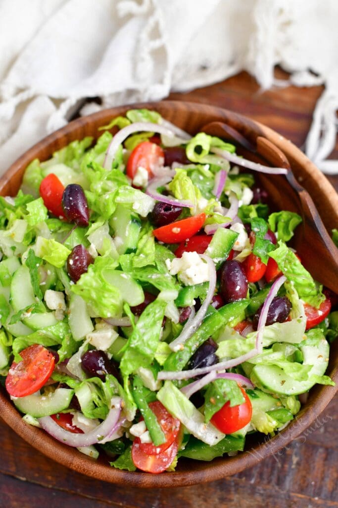 A tossed greek salad is in a large wooden bowl.