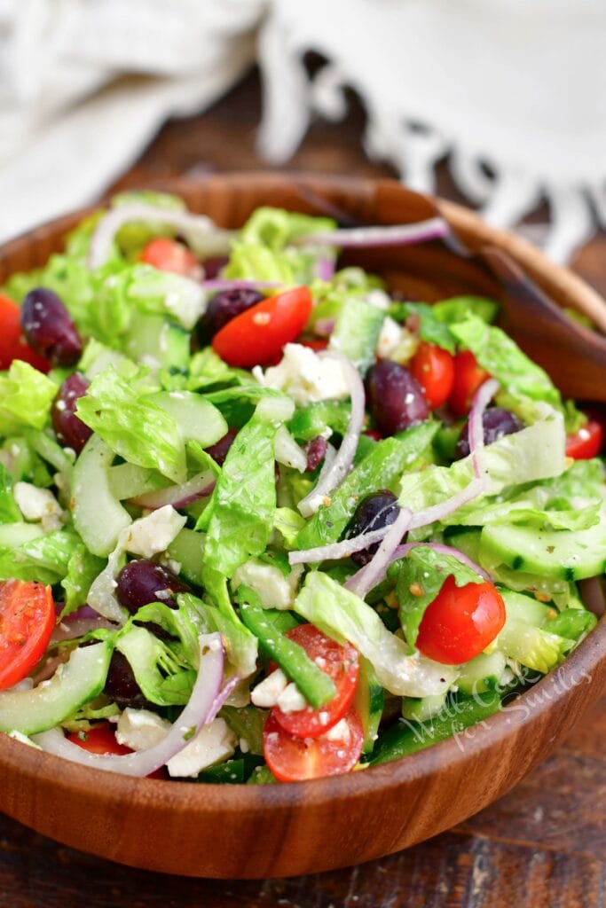 A greek salad in a large wooden serving bowl has been tossed and is ready to be served.
