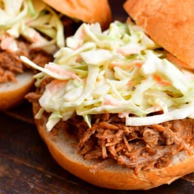 Coleslaw is sitting on a freshly made pulled pork sandwich.