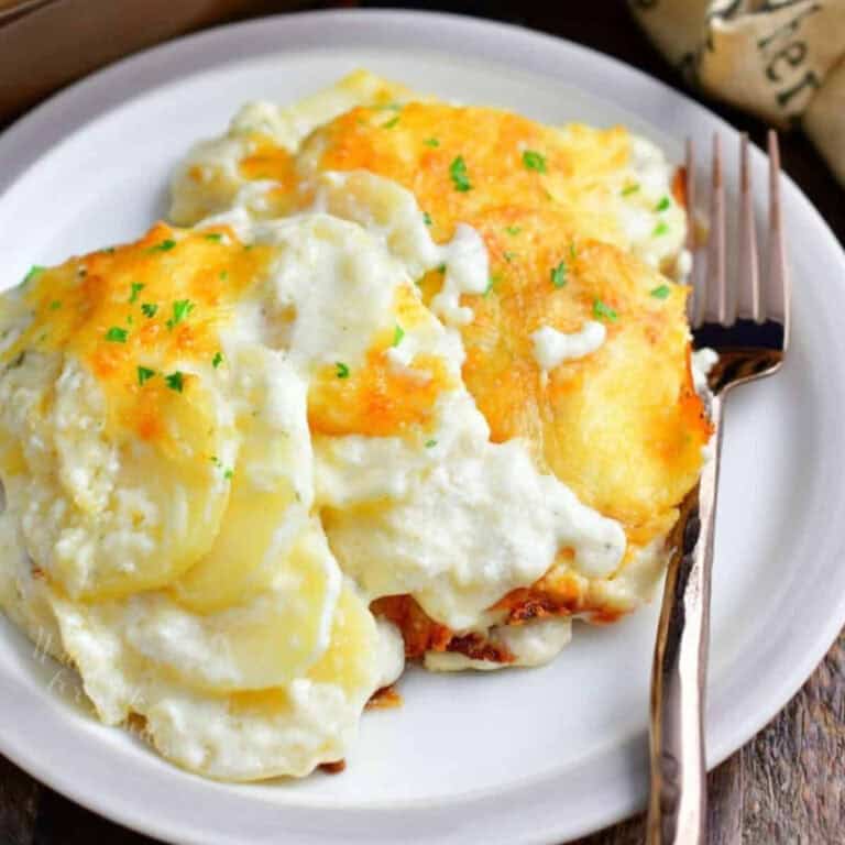 a portion of creamy and cheesy scalloped potatoes on a plate with a fork next to it.