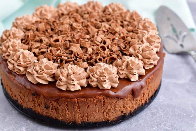 A chocolate cheesecake is covered with whipped cream and shaved chocolate.