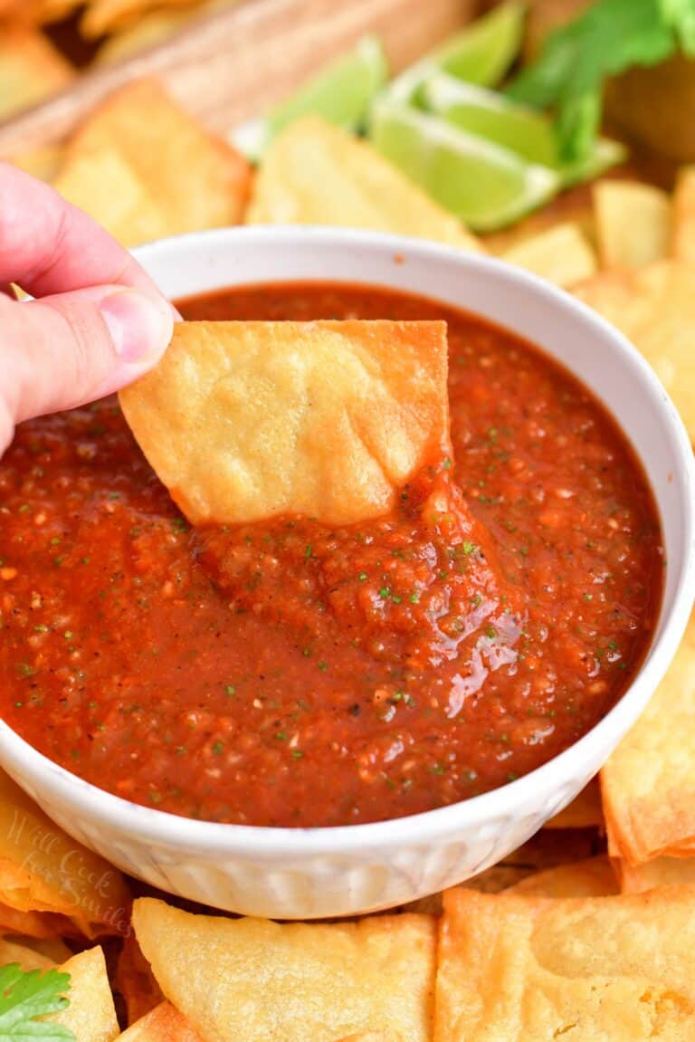 A chip is being dipped into red salsa.