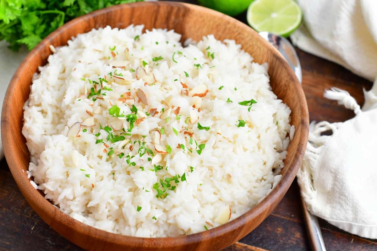 Coconut rice is presented in a wooden bowl and garnished with almonds and fresh herbs.