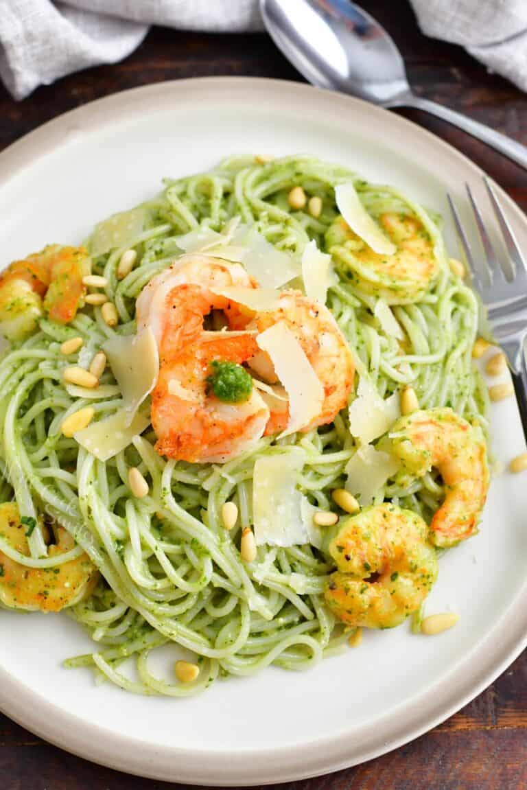 A white plate is filled with pesto pasta and shrimp.