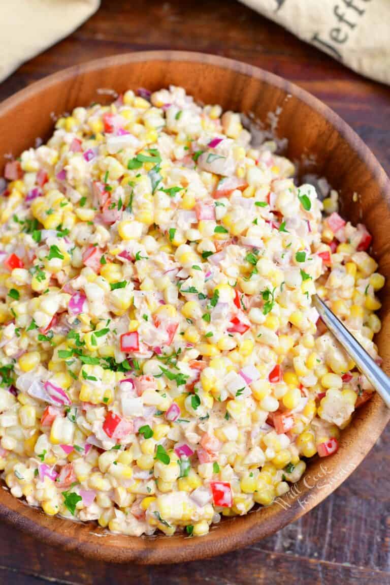 A large wooden serving bowl is filled with freshly made corn salad.