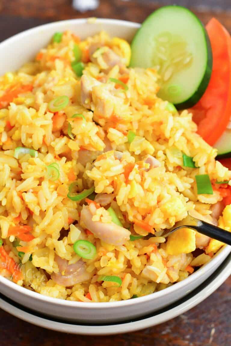 close up and scooping Thai fried rice in a bowl with cucumber and tomato slices