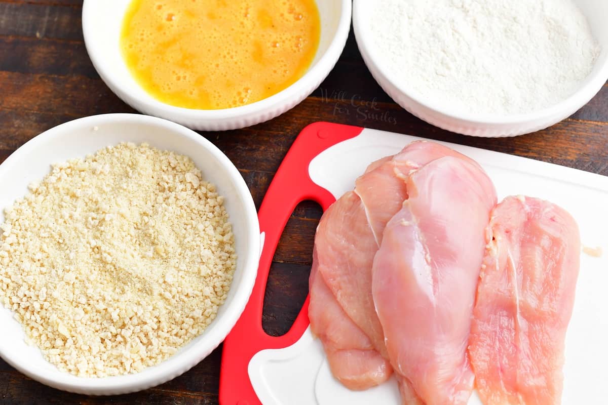 The ingredients for chicken milanese are plated on a wooden surface. 