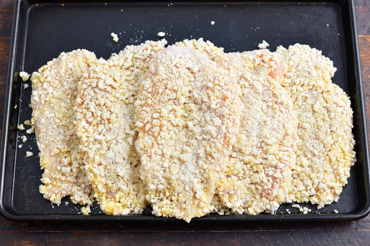 Several panko coated chicken breasts are on a black surface. 