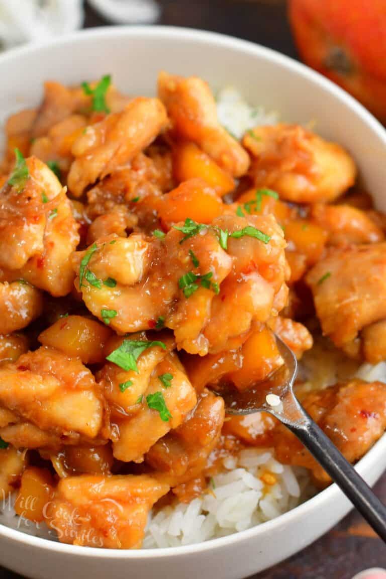 scooping some mango chicken with a fork from a bowl