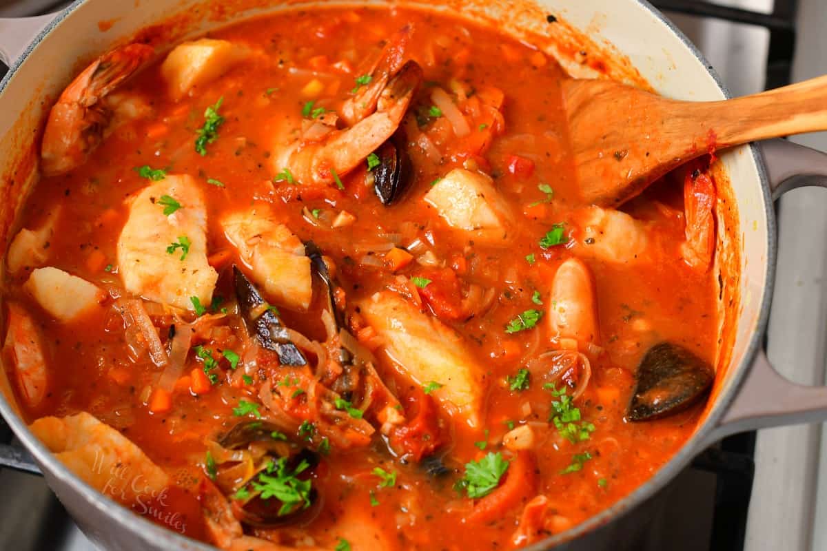 cooked Cioppino (seafood stew) in a pot on the stove with a wooden spoon.